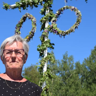 Kvinna står vid midsommarstång.