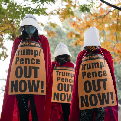 Kolme orjattaren asuun pukeutunutta mielenosoittajaa kaulassaan Trumpia ja Penceä vastustavat kyltit.