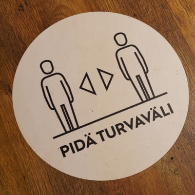 Ett klistermärke på ett golv som påminner om att man ska hålla säkerhetsavstånd.