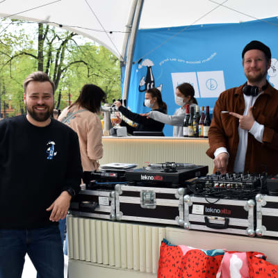 Två personer vid försäljningstält. Ena är DJ och pekar glatt på den andra.