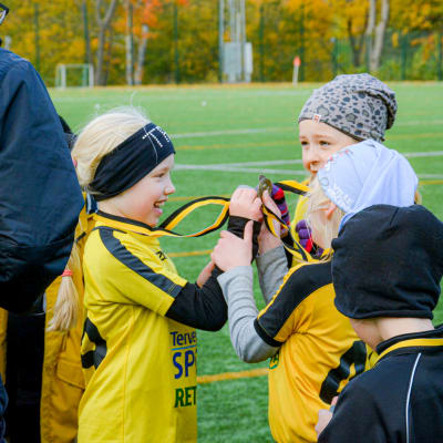 Fotbollsflickor glädjs över sina medaljer och visar upp dem för varandra.
