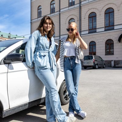 Porträttfoto av två flickor på en skolgård som lutar sig mot en mopedbil