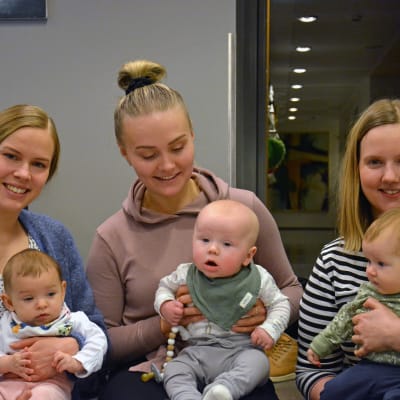 Tre mammor sitter på ett golv med sina små bebisar i famnen.