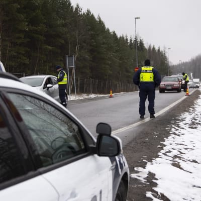 En landsväg med flera bilar som stannat och poliser i gula västar. Det finns lite snö på marken. Polisen övervakar den nyländska landsskapsgränsen.