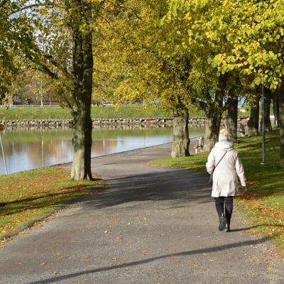 Kvinna går längs en stig nära vattnet i en vacker höstdag.