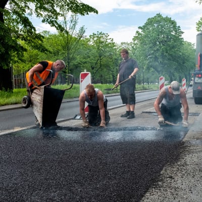 Fyra män arbetar med att asfaltera en väg.