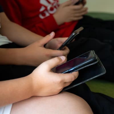 Barn som sitter i en soffa och ser på sina mobiltelefoner. Man ser bara armarna och händerna på barnen.