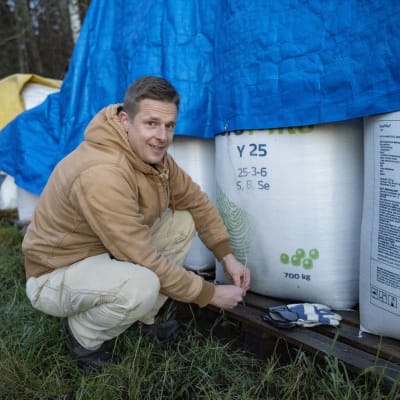 Jordbrukaren Kristofer Örnmark i Ingå sitter på huk invid konstgödselsäckar. 