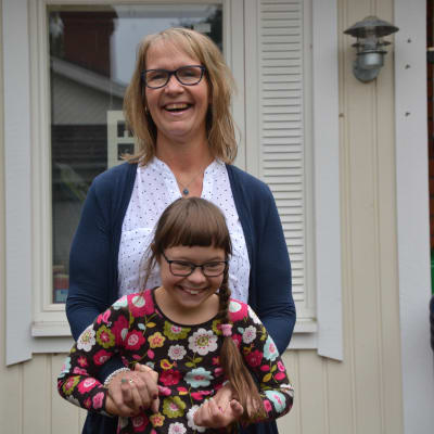 Maria Backman står med dottern Lotta framför sig utanför deras hus. Båda ler. 
