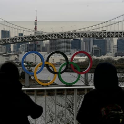 Två personer står och tittar på de olympiska ringarna i Tokyo