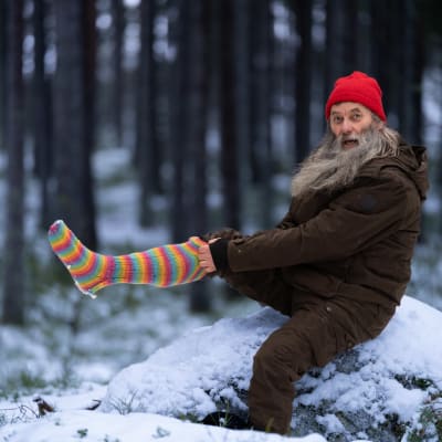 Ilvesmies Hannu Rantala vetää villasukkaa jalkaan lumisessa metsässä.