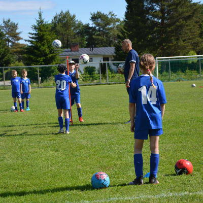 Unga flickor och pojkar kastar en fotboll sinsemellan på en fotbollsplan. 