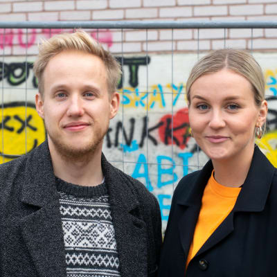 Simon Karlsson och Märta Westerlund poserar framför staket och graffitivägg på Yles gård.