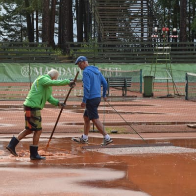 Två män torkar upp en regnvåt tennisbana.
