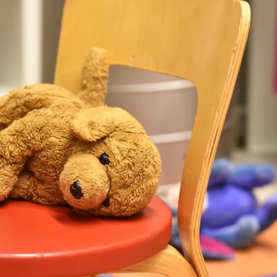 En leksakshund ligger på en barnstol vid ett rött barnbord. I bakgrunden ligger en leksaksåsna.