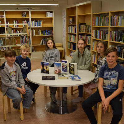 Dag Bahér, Casper Malmsten, Birna Hampf, Lovisa Lindbom, Alma Lindholm. Rudi Viljanen sitter vid ett bord i biblioteket i Degerby skola. 