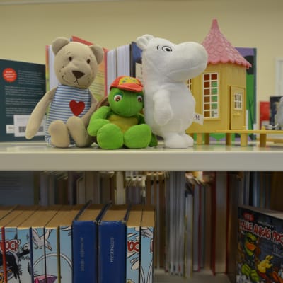 En hylla i ett bibliotek, med böcker och gosedjur.