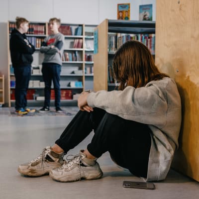 En elev sitter på golvet i ett skolbibliotek.
