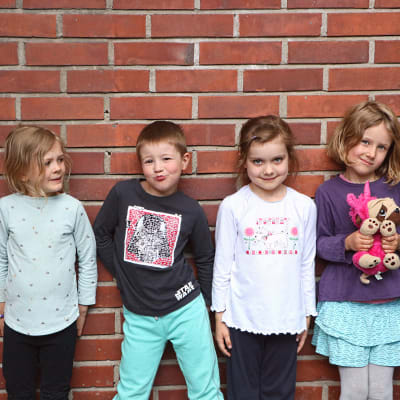Fyra barn i dagisåldern står framför en tegelvägg.
