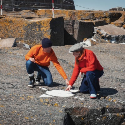 Man och kvinna pekar på bild av kompass som målats på en klippa.