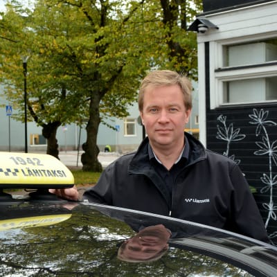Taxichaufför står vid sin bil.