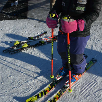 En utförsåkare står färdig med skidor och stavar påsatta.