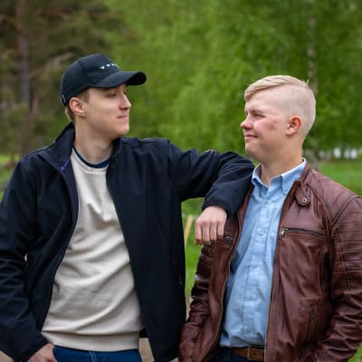 Kaksi nuorta miestä, Juuso Mäkinen ja Akseli Moisio seisovat soratiellä ja katsovat hymyillen toisiinsa. Juuso nojaa kädellään Akselin olkapäähän. 