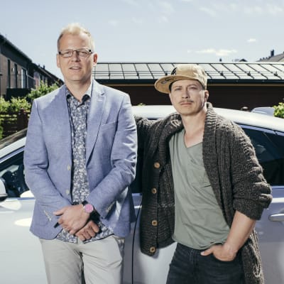 Luottomiehen Juhis (Kari Ketonen) ja Tommi (Antti Luusuaniemi) seisovat vierekkäin vaaleaan autoon nojaten kotipihassaan katsoen kameraan.