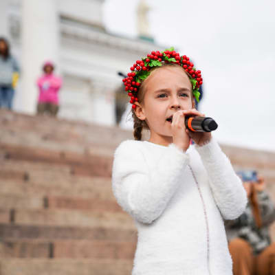 Sjuårig flicka sjunger i en mikrofon på Domkyrkans trappa i Helsingfors. 