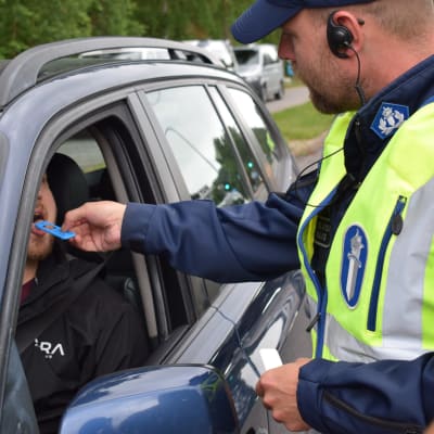 Polis utför ett blårstest för bilist som sitter i sin blåa bil.
