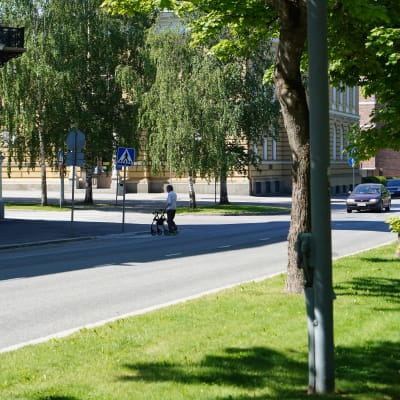 Nainen ylittää tietä rollaattorin avulla. Auto lähestyy taustalla.