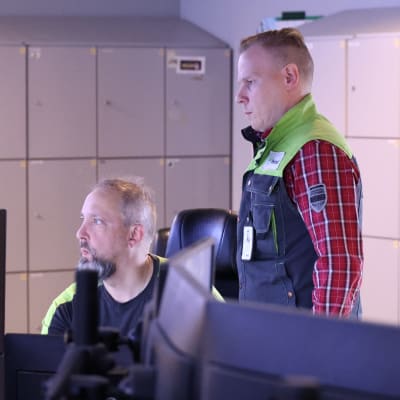 Två män i ett kontrollrum kollar på skärmar