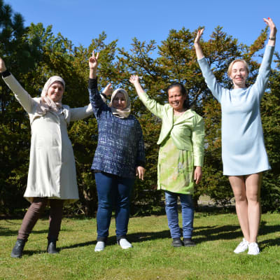 fyra kvinnor av olika nationalitet glada mot grön gräsmatta och blå himmel i solsken