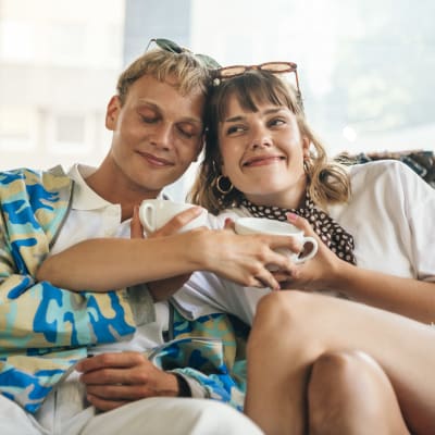 Oona (Anna Airola) ja Arttu (Elias Salonen) istuvat iloisina vierekkäin sohvalla toisiinsa nojaten.
