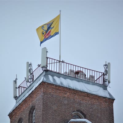 Flagga med Jakobstads stadsvapen vajar i toppen av ett torn.
