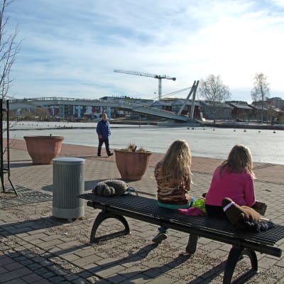 Två flickor som sitter på en parkbänk och tittar ut över Borgå å.