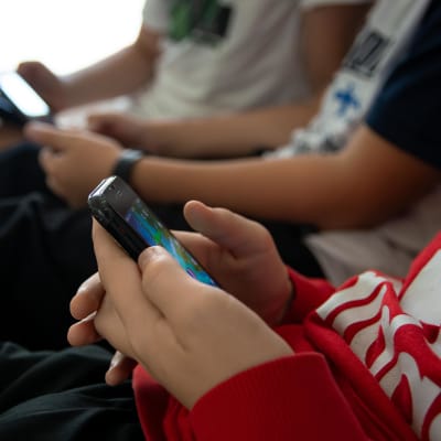 Tre pojkar som sitter bredvid varandra i en soffa och scrollar på sina smarttelefoner.