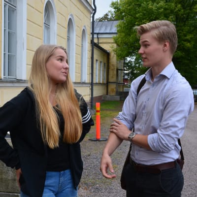 en flicka och en pojke står och pratar med varandra utanför ett gymnasium