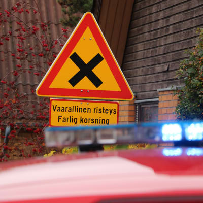 Ett trafikmärke som varnar för farlig korsning. I förgrunden syns taket av en brandbil med blinkande ljus.