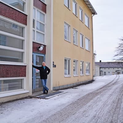 John Rönnholm står vid huvudingången till det nya hotellet. Beige rappat hus i tre våningar med blå dörr. 