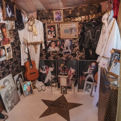 Rum med mycket Elvis Presley-relaterade saker: bilder, en gitarr, en docka i miniatyr, två vita dräkter. På golvet en stjärna målad i guldfärg samt texten Elvis Presley.
