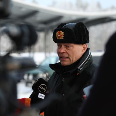 Vartiuksen rajavartioaseman päällikkö, kapteeni Jouko Kinnunen haastattelussa, ympärillä ihmisiä ja mikrofoneja edessään.