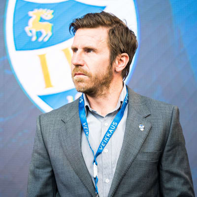 Daniel Norrmén i grå kostym med IFK Mariehamns logo bakom sig.