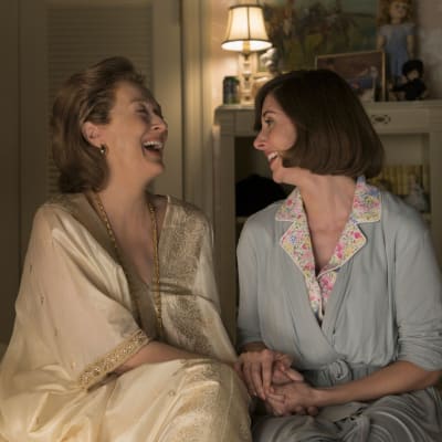 Katharine Graham (Meryl Streep) och dottern Lally Graham (Alison Brie) sitter bredvid varandra på sängen och skrattar.