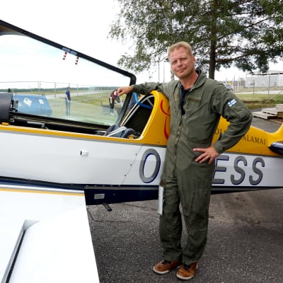 Man i grön flygdräkt står lutad mot ett flygplan.