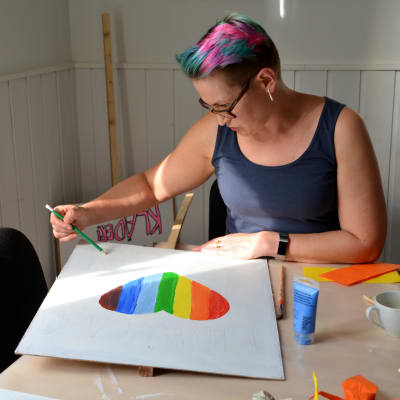 En kvinna målar ett hjärta i regnbågensfärger