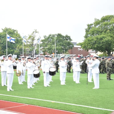 Militärorkester i vitt ute på sportplan.