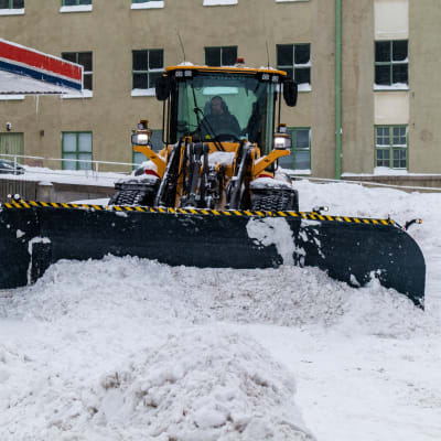 Traktor röjer snö på gård.