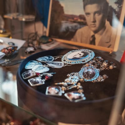 Smycken med bilder av Elvis Presley, i bakgrunden ett porträtt på Elvis Presley.