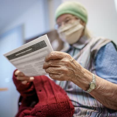 Äldre dam håller i sitt vaccinbevis.